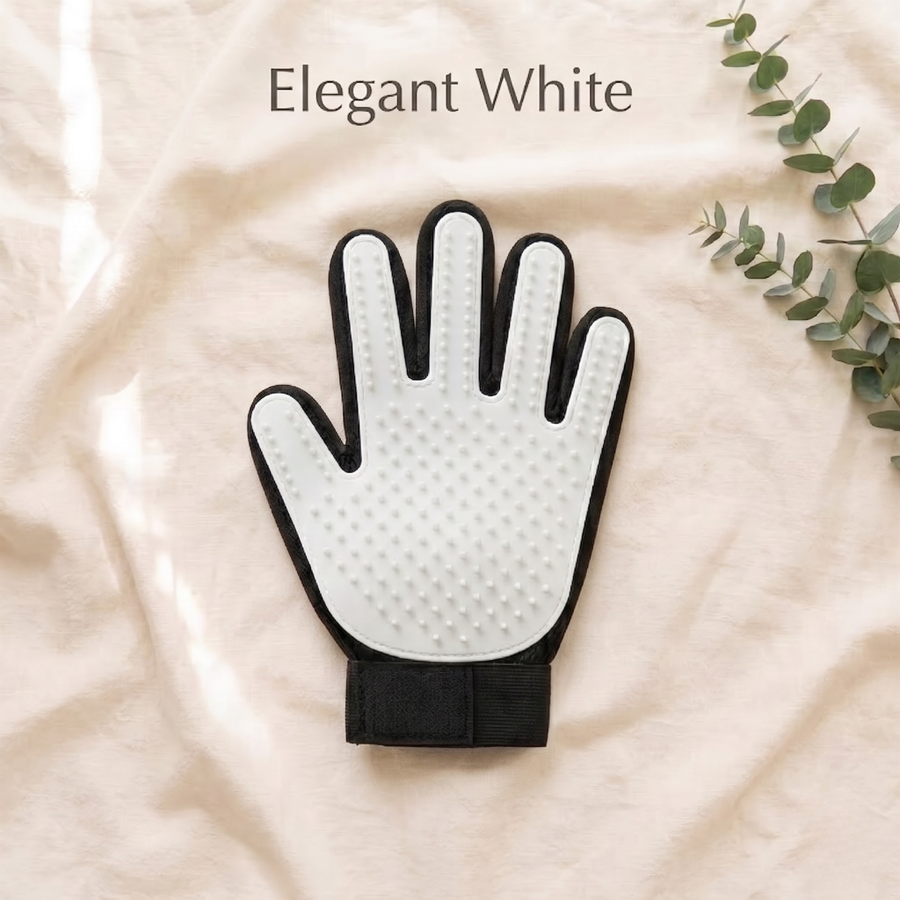 A hand-shaped grooming glove in 'Elegant White' with a textured white palm and black edges, displayed on a beige fabric background with a sprig of eucalyptus.