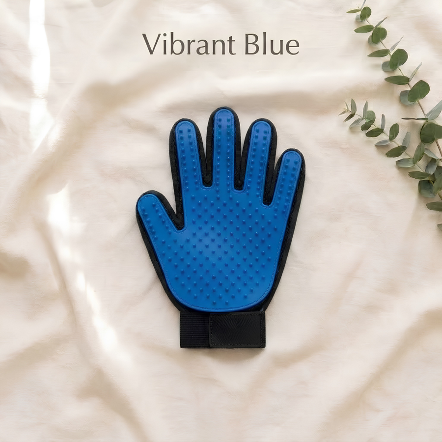 A blue hand-shaped grooming mitt with black trim and a black wrist strap, laid flat on a cream fabric background with the text 'Vibrant Blue' above it and eucalyptus leaves in the corner.